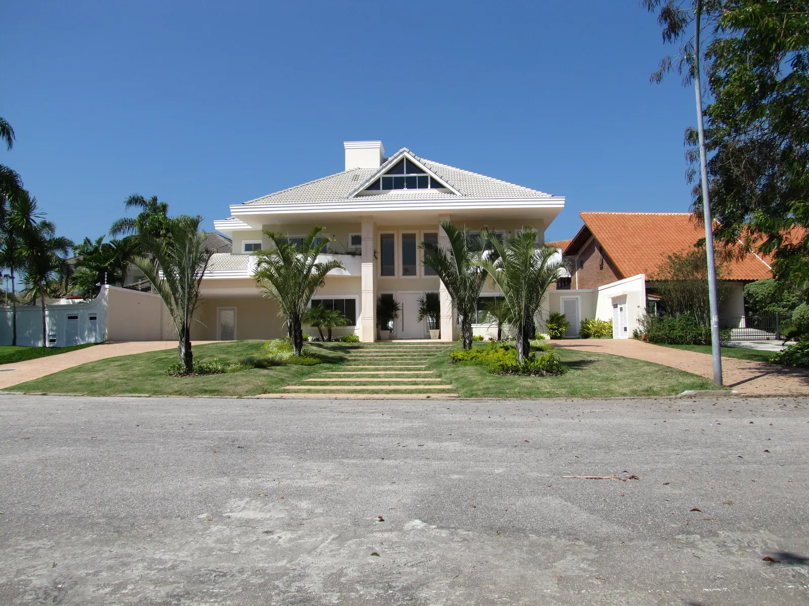 Casa clássica entregue pela BRC, com telhado claro, coqueiros e jardim frontal