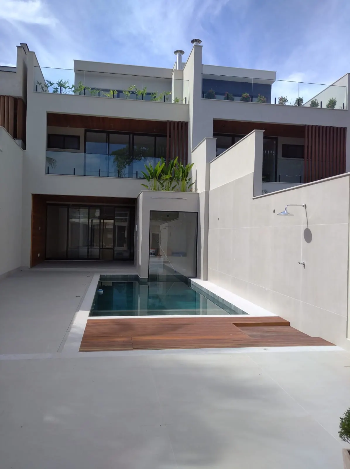 Área de lazer de casa entregue pela BRC, com piscina, deck de madeira e fachada de três pavimentos