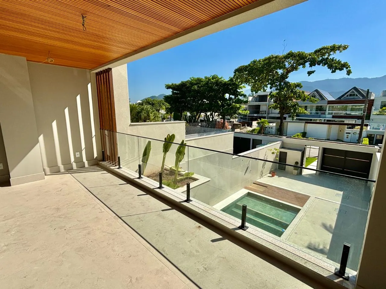 Varanda com forro de madeira e guarda-corpo de vidro, vista para a piscina e a montanha